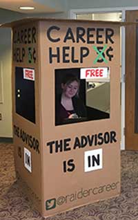 Photo of Wright State University Career Center advisor inside the portable, cardboard box titled "Career Help" (5 cents crossed out, hanging sign says "free"), "The advisor is in." Includes Twitter handle @raidercareer. 