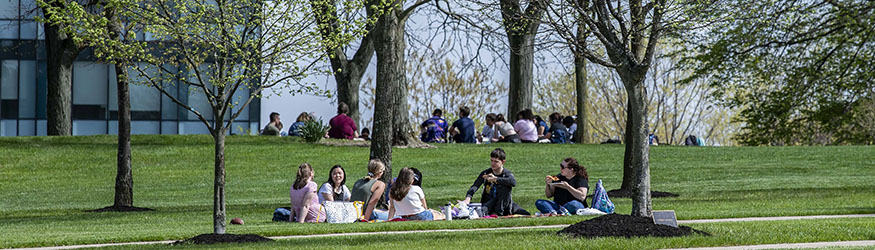 photo of students sitting in a circle on the grass outside on campus